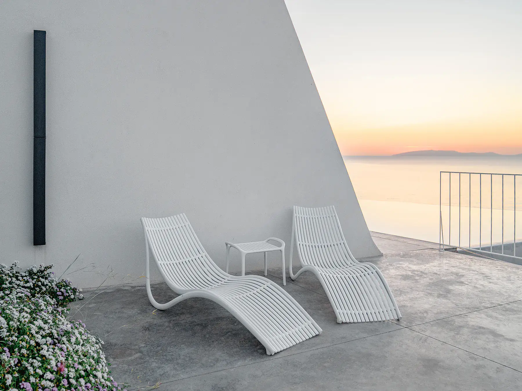 Minimalist white terrace with sculpted loungers and panoramic sea view.