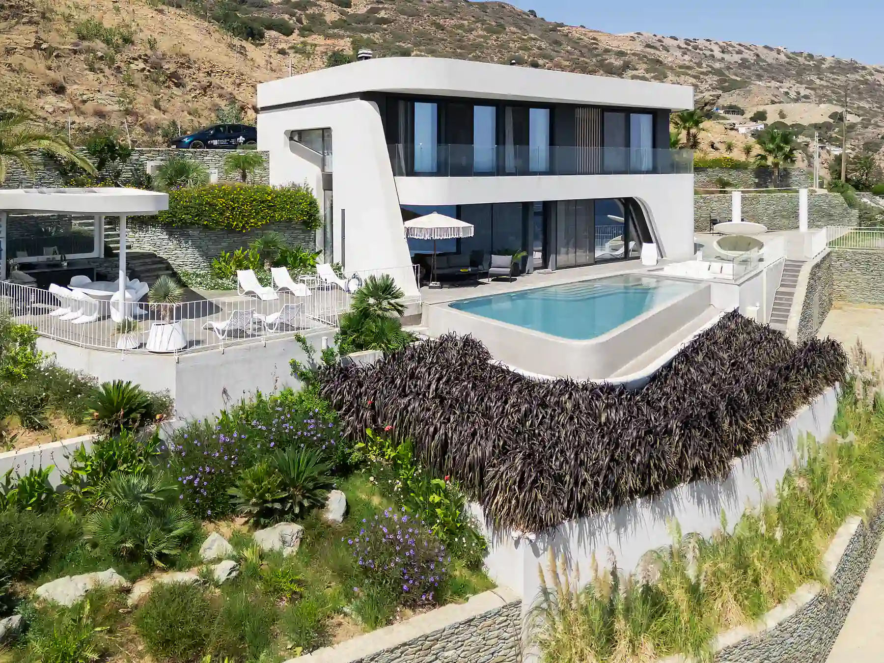 Aerial view of Meltemi Villa with infinity pool and landscaped gardens overlooking the sea.