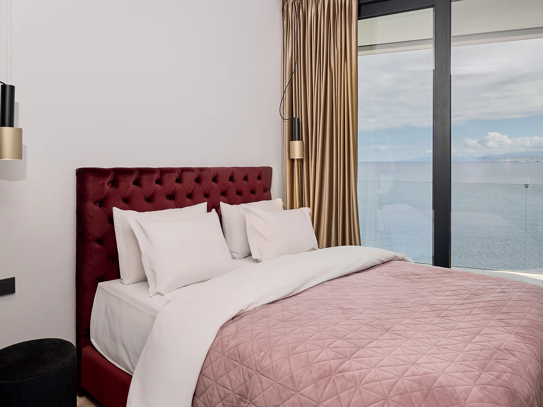 Bright bedroom with plush headboard and large glass doors opening to a sea-view terrace.