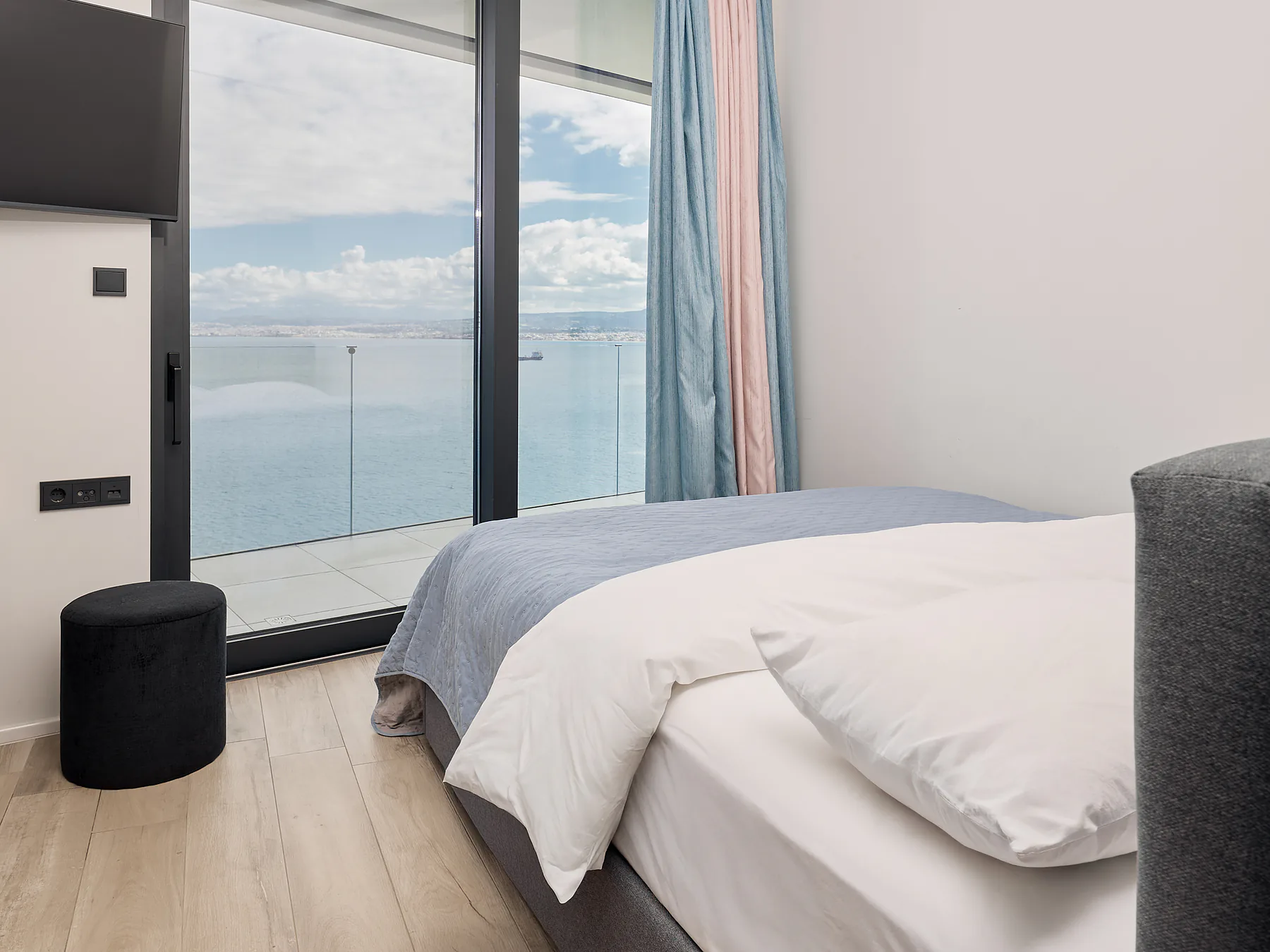 Minimalist bedroom with soft blue tones and balcony overlooking the Aegean Sea.