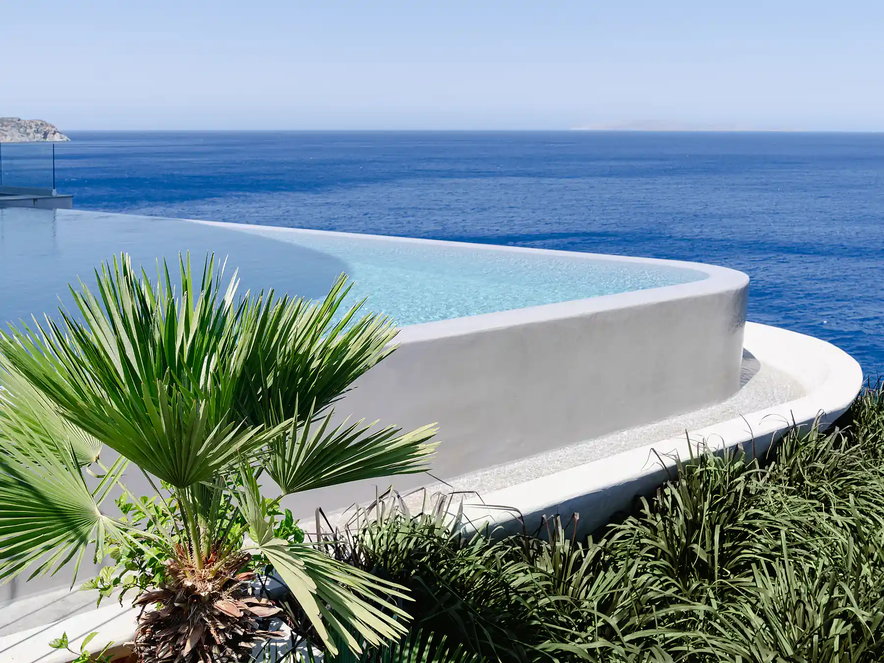 Luxury infinity pool surrounded by palms overlooking the deep blue Mediterranean.