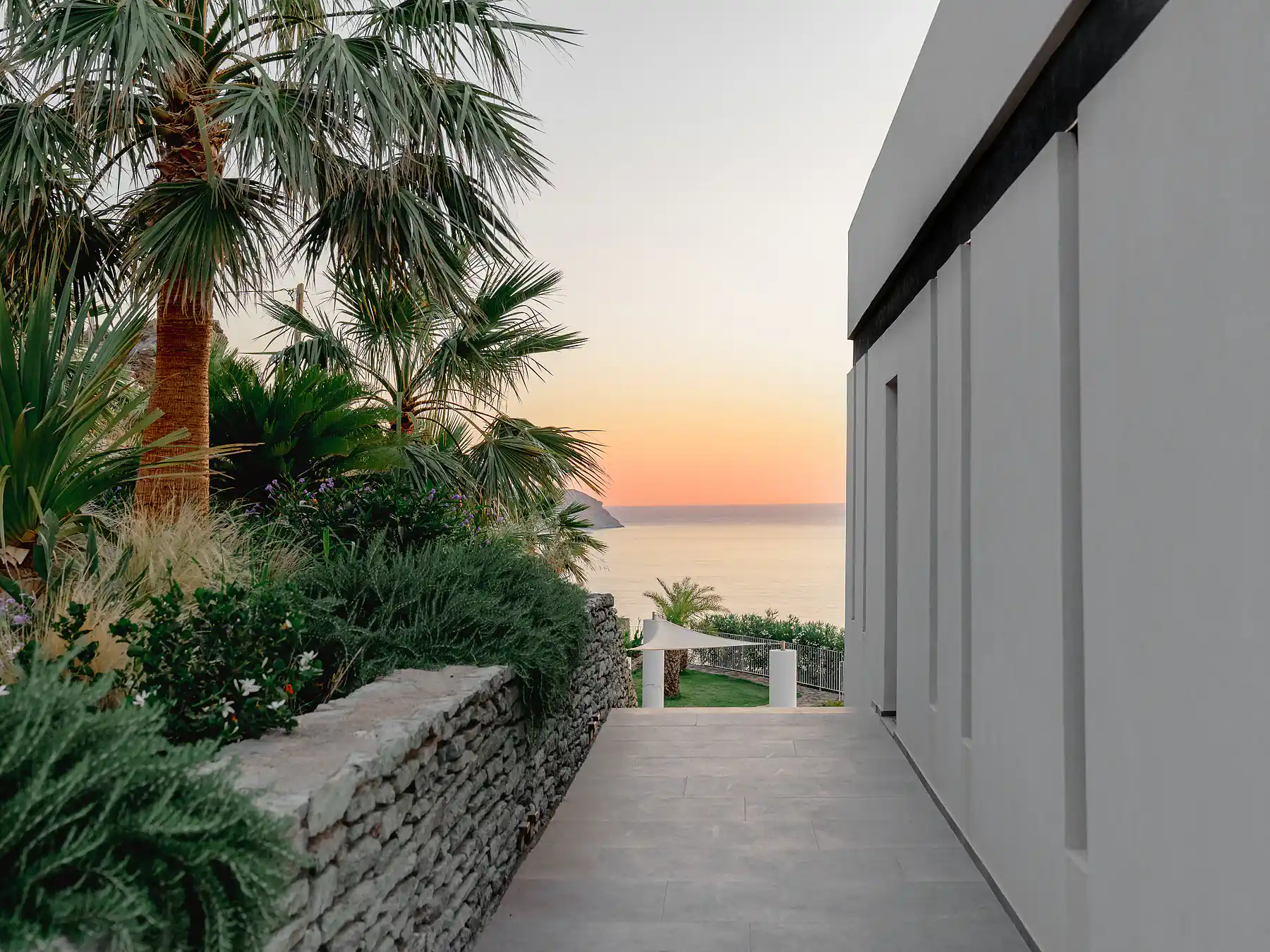 Stone pathway framed by greenery leading to sea-view terrace at sunset.