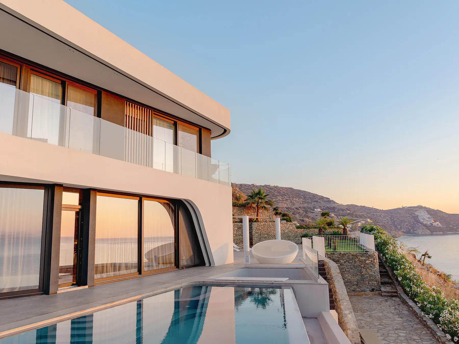 Modern villa exterior with curved lines and pool reflecting the surrounding landscape.